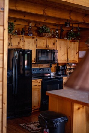 A kitchen with wooden cabinets, a black refrigerator, a microwave, and a stove. - Overwatch: HUGE Game Room, Hot Tub, FirePit, &More (Pigeon Forge)