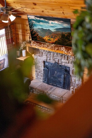 A stone fireplace with a decorative metal screen, a television mounted above it, and a window with curtains. - Overwatch: HUGE Game Room, Hot Tub, FirePit, &More (Pigeon Forge)