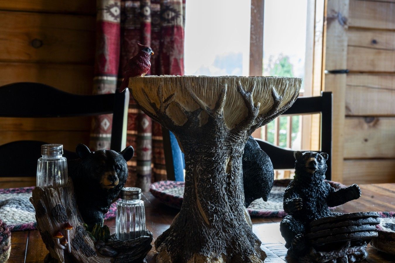 A rustic wooden table with a carved tree centerpiece, two bear figurines, and salt and pepper shakers.