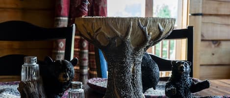 Una mesa de madera rústica con un centro de mesa tallado con forma de árbol, dos figuras de osos y saleros y pimenteros.