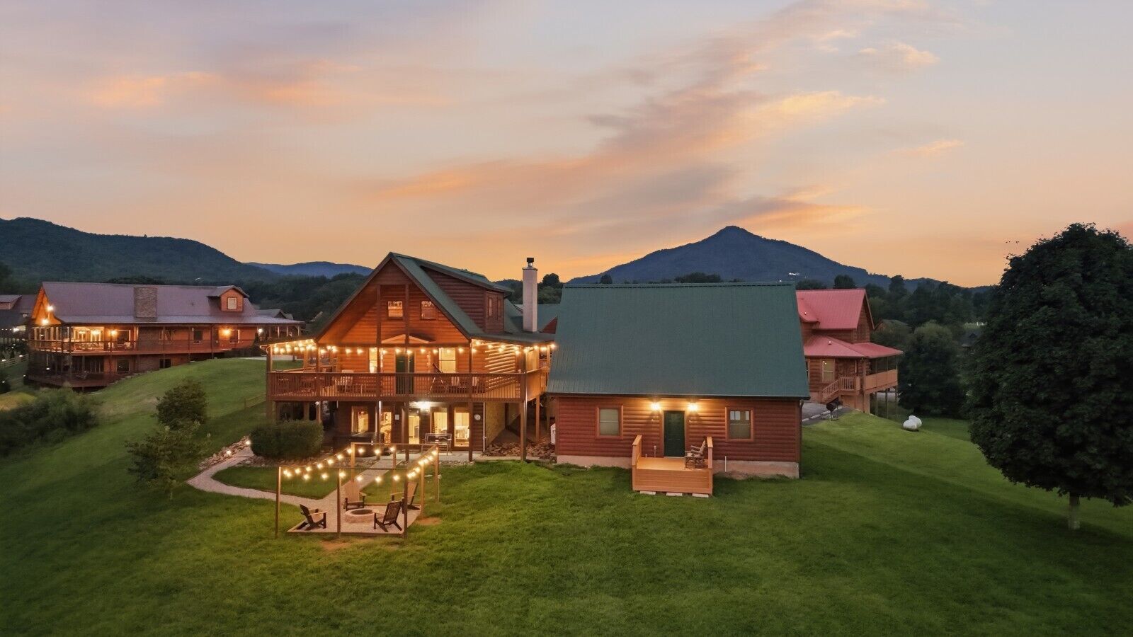 A large lodge with a two-story main building and a smaller attached structure, surrounded by a well-maintained lawn and a mountain in the background.