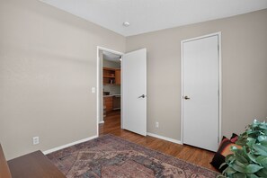 A hallway with a patterned rug, a closed door, and an open door leading to a kitchen area. - Cozy AZ Desert Escape – Hiking, OHV & Mtn Views (Black Canyon City)