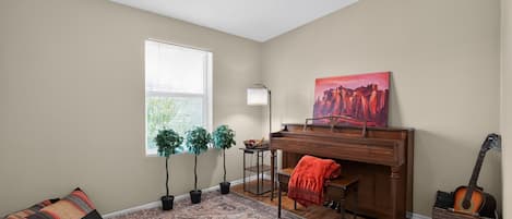 Ein Zimmer mit einem Klavier, einer Gitarre, einem Gemälde, einer Lampe und zwei Blumentöpfen.