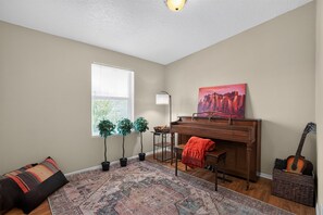 A room with a piano, a guitar, a painting, a lamp, and two potted plants. - Cozy AZ Desert Escape – Hiking, OHV & Mtn Views (Black Canyon City)