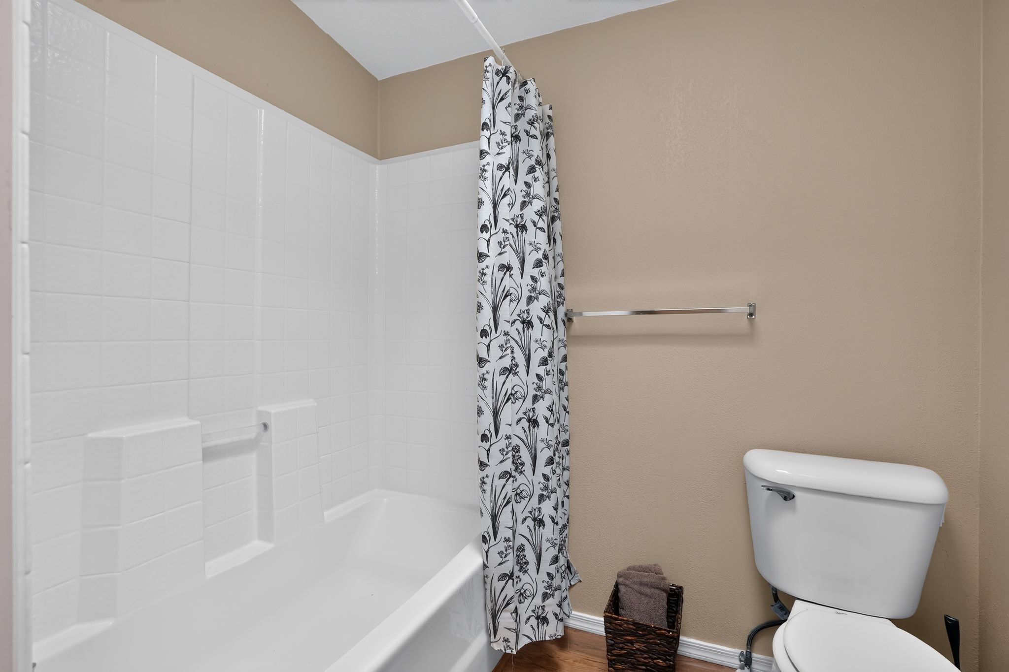 Un baño con una bañera blanca, un inodoro y una cortina de ducha con estampado floral.
