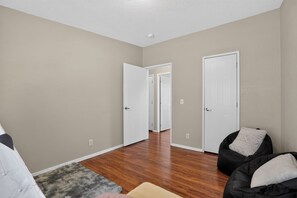 Una habitación amplia con suelo de madera, un alfombra mullida gris y un sillón informal negro.