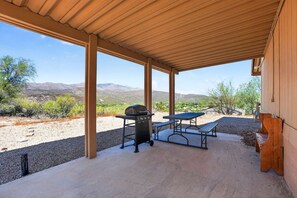 An outdoor patio with a barbecue grill and a picnic table, surrounded by a desert landscape and mountains. - Cozy AZ Desert Escape – Hiking, OHV & Mtn Views (Black Canyon City)