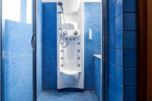 A bathroom with blue-tiled walls, a white bathtub, and a showerhead. - Vrbo Property (Catania)