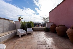 Eine Terrasse mit Steinboden, zwei weißen Kunststoffstühlen, Terrakottatöpfen und einer roten Wand.