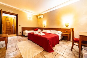 A hotel room with a bed, two bedside tables, a desk, and a chair. There are two wall-mounted lamps and an air conditioning unit. - Vrbo Property (Catania)