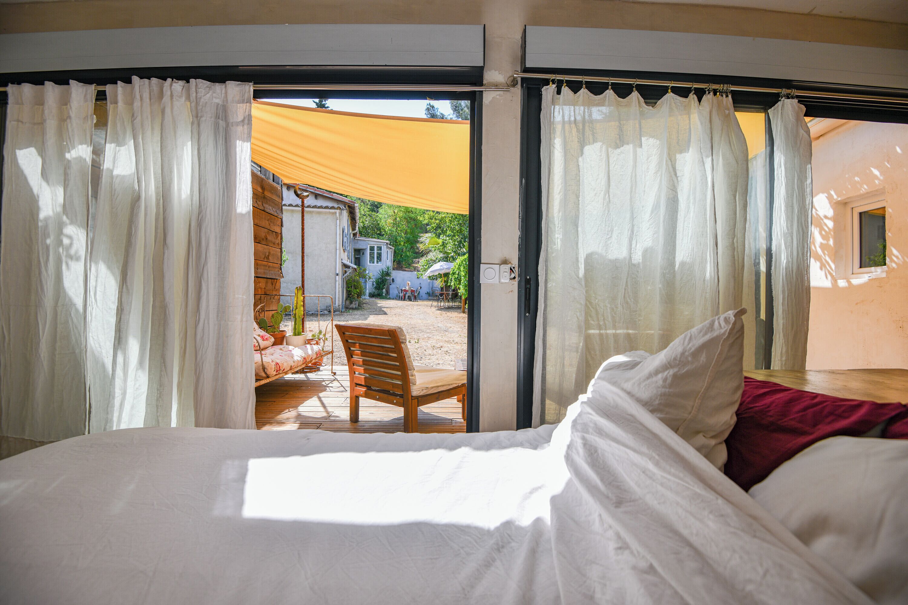 A bedroom with a bed, white curtains, and a view of an outdoor patio area.