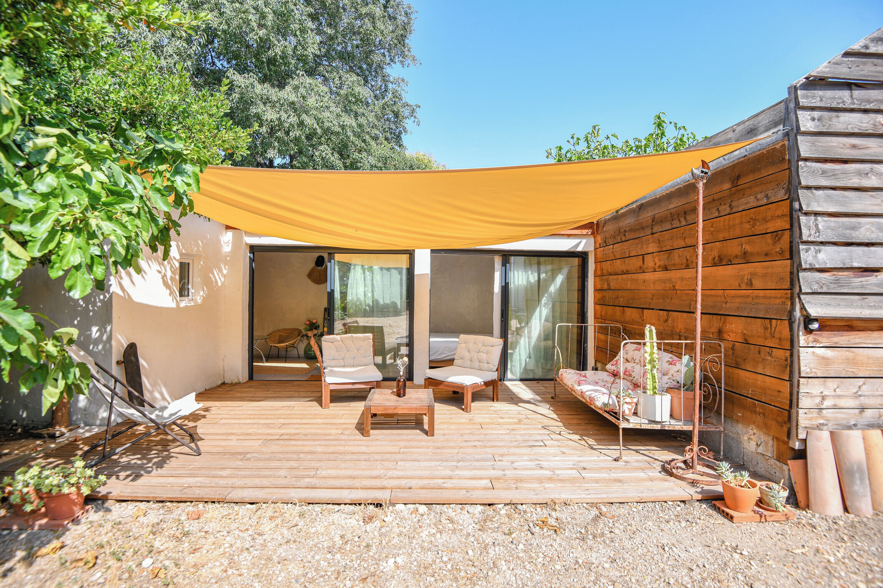A wooden deck with outdoor furniture, a yellow shade, and potted plants.