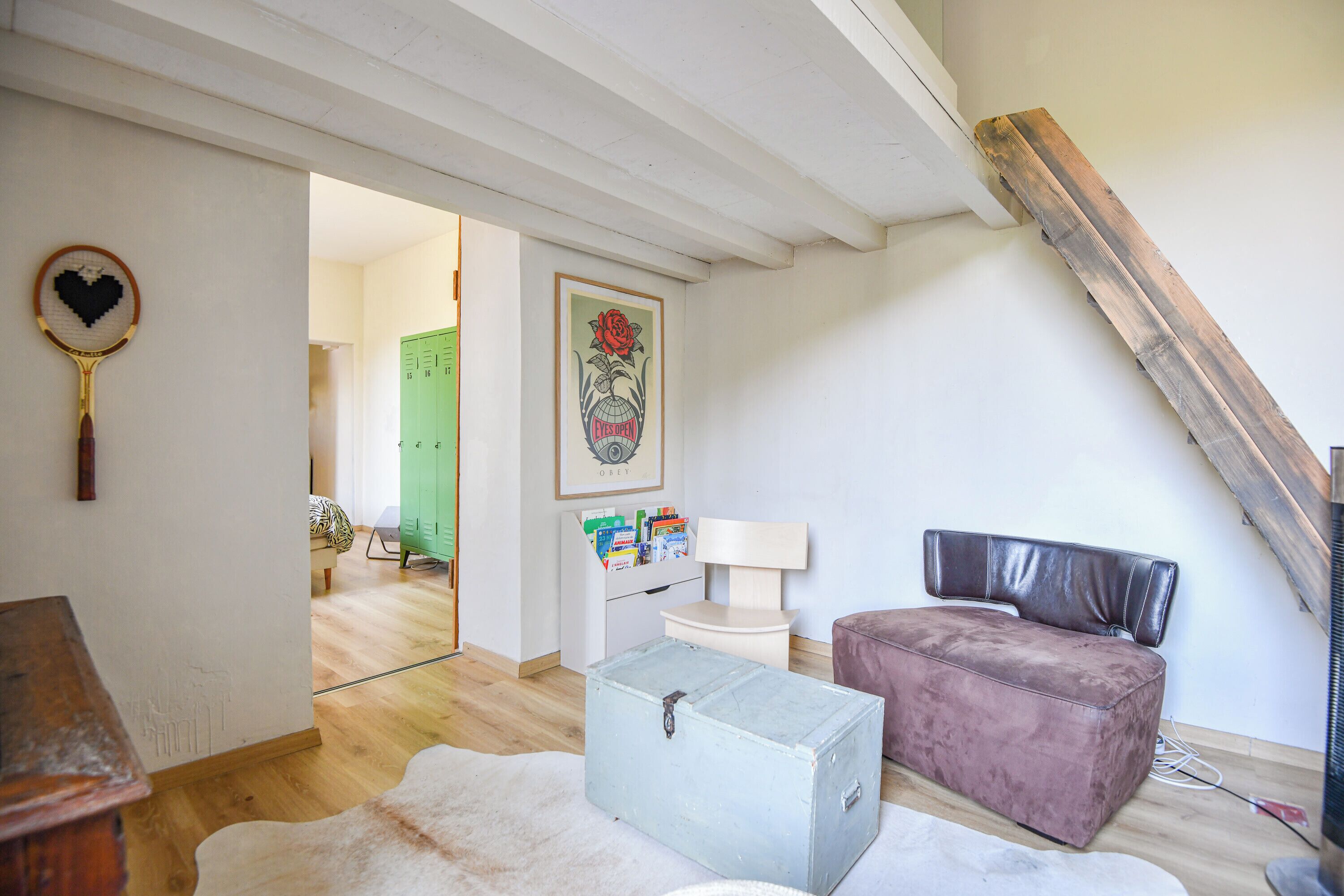 A room with a loft bed, a small table, a green locker, a framed picture, and a white cabinet.