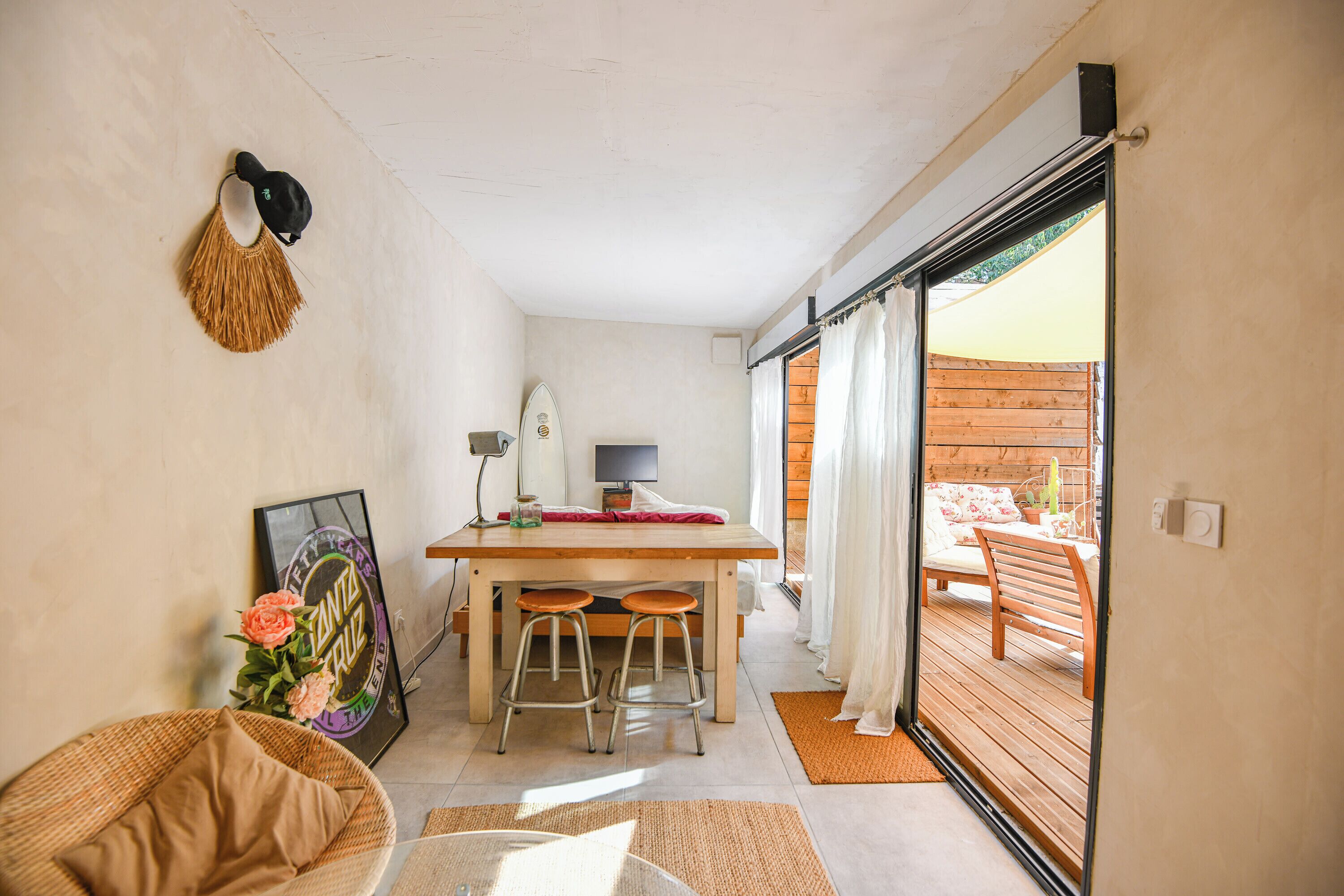 A room with a wooden table, two chairs, a desk with a computer, a framed picture on the wall, and a sliding glass door leading to an outdoor area.