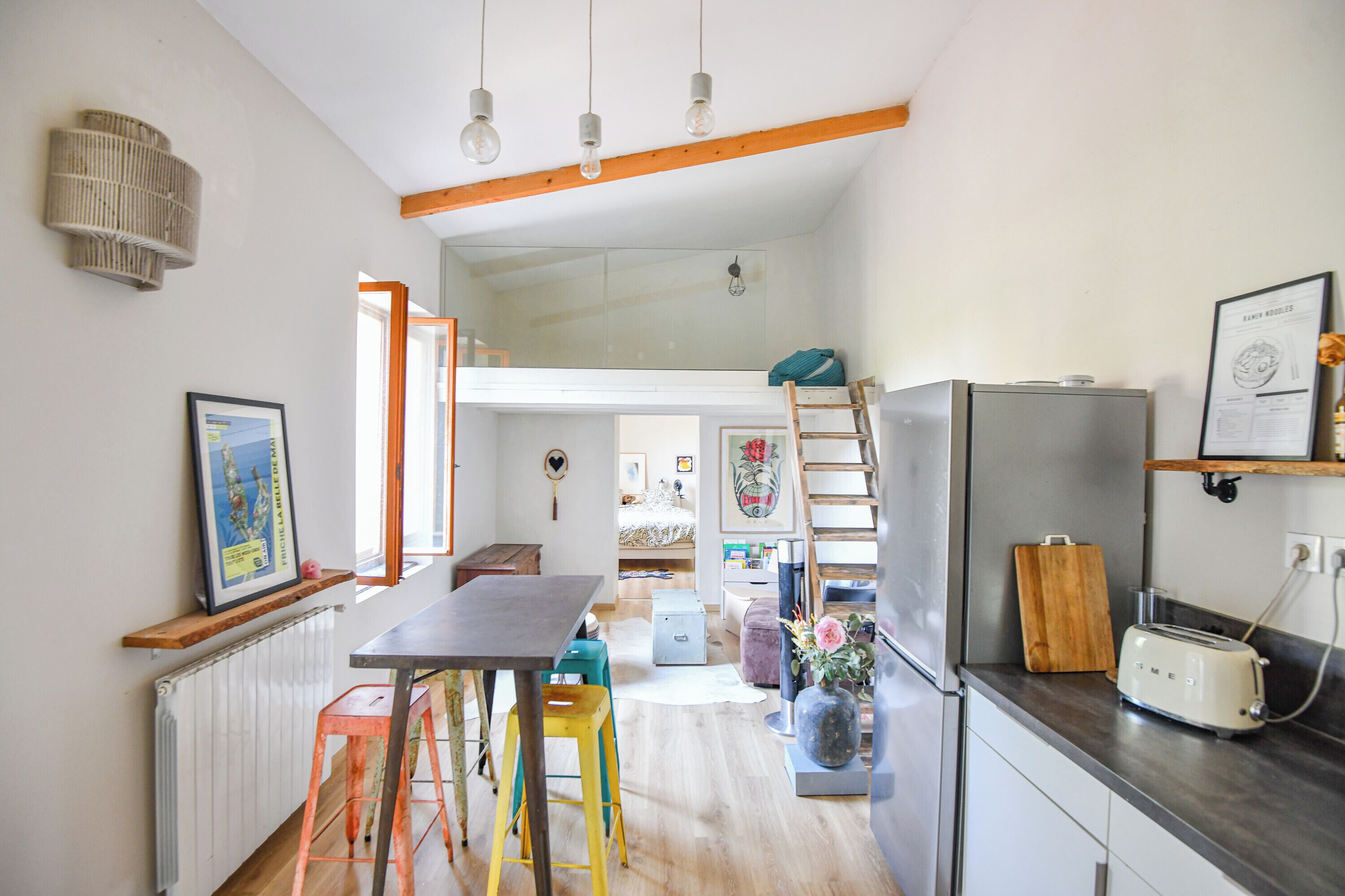 A kitchen with a wooden table, stools, a refrigerator, and a ladder.