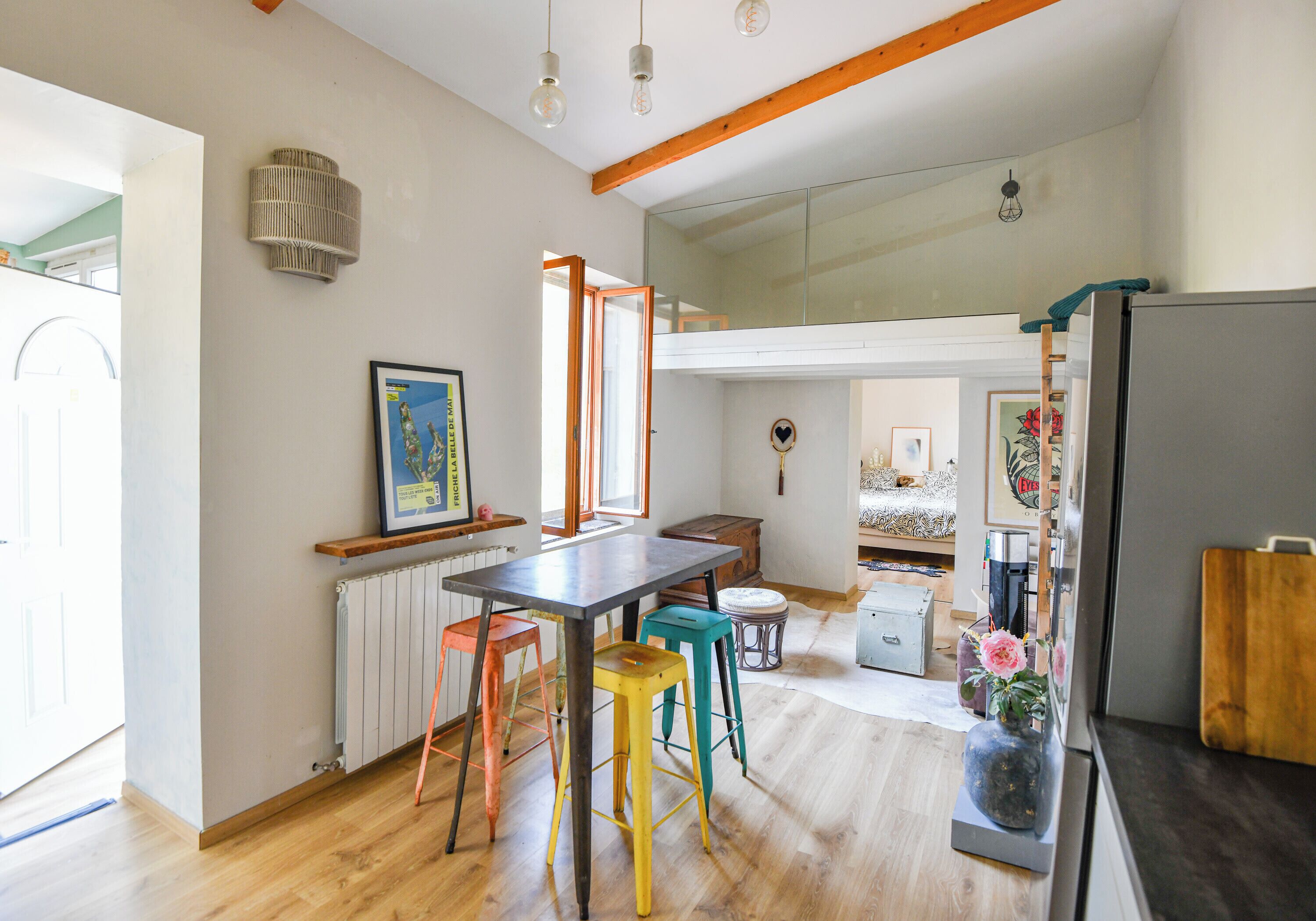A kitchen with a wooden table, colorful stools, a radiator, and a refrigerator.