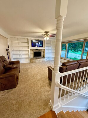 A living room with a fireplace, a television, and a staircase. - EV charger modern 4 bedroom, 3 Bathroom house in great neighborhood Cedar Rapids (Cedar Rapids)