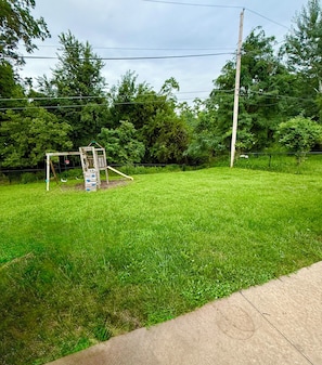 A grassy yard with a wooden play structure and a concrete path.