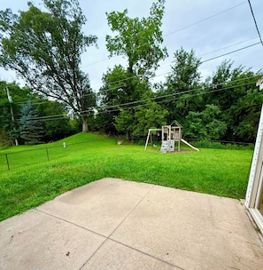 A backyard with a concrete patio, a swing set, and a fenced area.