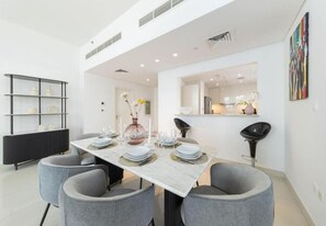 A modern dining area with a white table set for four, grey chairs, and a black console with decorative items. - BLVD Crescent Tower 1 (Dubai)
