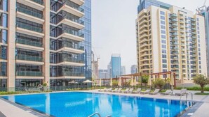 A swimming pool with lounge chairs and a view of high-rise buildings. - BLVD Crescent Tower 1 (Dubai)