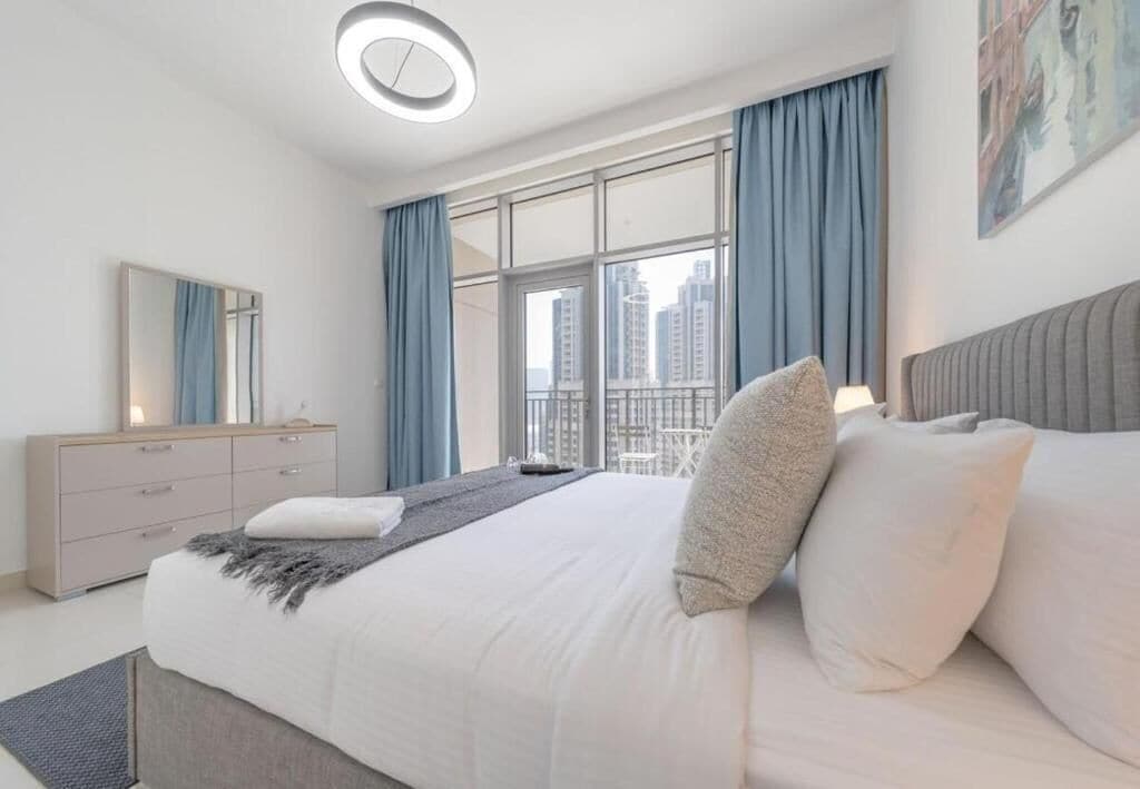Une chambre moderne avec un grand lit, une commode et une vue sur la ville grâce à de grandes fenêtres.