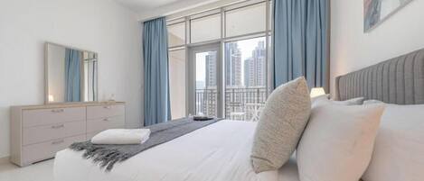 Quarto moderno com uma cama grande, um aparador e vista para a cidade através de amplas janelas.