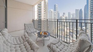 A balcony with a city view, cushioned seating, and a table with a plate of food. - BLVD Crescent Tower 1 (Dubai)