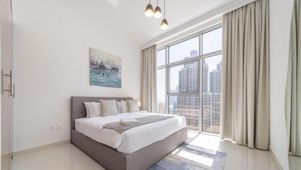 A modern bedroom with a large bed, a city view, and a painting on the wall. - BLVD Crescent Tower 1 (Dubai)