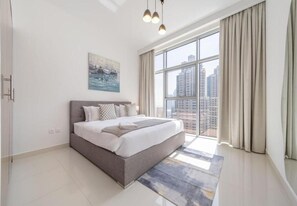 A modern bedroom with a large bed, a city view, and a painting on the wall. - BLVD Crescent Tower 1 (Dubai)