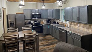 A modern kitchen with wooden ceiling, stainless steel appliances, and a dining area with a table and chairs.