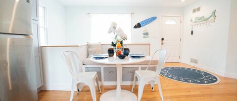 A modern kitchen with white cabinetry, a stainless steel refrigerator, a round dining table with two white chairs, and a blue decorative rug on the floor.