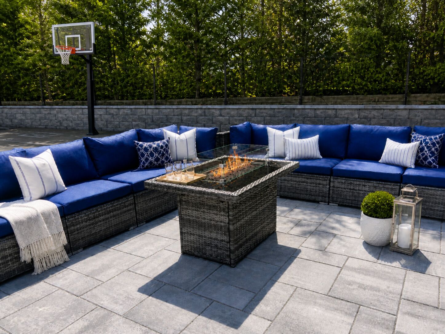 An outdoor seating area with a fire pit table, blue sofas, and a basketball hoop.