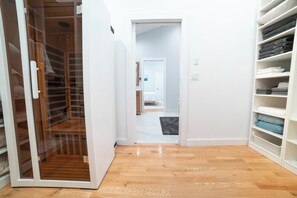 A hallway with a wooden floor leading to a room with a bed and a bathroom. - Hampton Bays Resort-Style Retreat with Pool, Hot Tub, Basketball & Pickleball! (Hampton Bays)