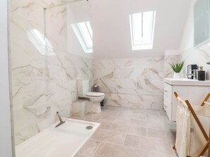 Ein Badezimmer mit Marmorwänden, einer Toilette, einer Dusche und einem Waschbecken mit Spiegel.