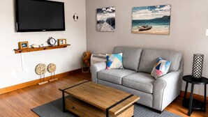 A living room with a grey sofa, wooden coffee table, and two wall-mounted paintings. - Missy By The Sea, Harbour View Suite (Twillingate)