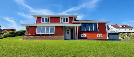 A two-story house with a red exterior, a brick foundation, and a well-maintained lawn.