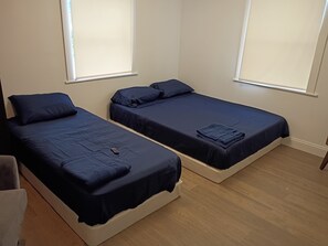 Two single beds with dark blue bedding, wooden flooring, and white walls. - Vrbo Property (North Miami)