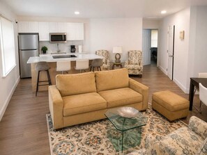 A modern living room with a sofa, ottoman, and glass coffee table. - Vrbo Property (North Miami)
