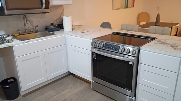 A modern kitchen with white cabinetry, a stainless steel stove, and a marble countertop. - Vrbo Property (North Miami)