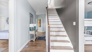 Una escalera con escalones de madera y barandilla blanca que lleva a un dormitorio con literas.