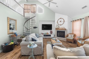 A spacious living room with a fireplace, a television, and a staircase. - "Whispering Palms"5 bed/3.5bath w/pool/beach access (North Topsail Beach)