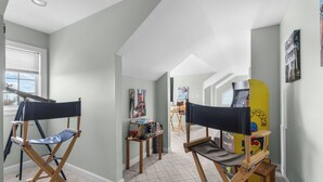 Una habitación con dos sillas plegables, un ventanal con persianas y una pared con cuadros.