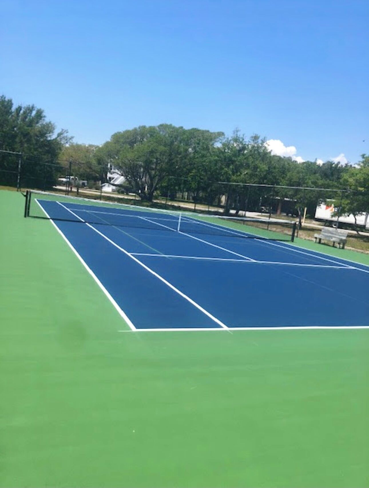 A tennis court with a net, surrounded by trees and a clear sky.