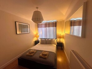 A hotel room with a bed, two bedside lamps, a large mirror, and a framed picture on the wall. - 2-Bed Flat in Shoreditch, Heart of Brick Lane (London)