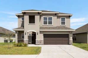 A two-story house with a garage, a small porch, and a stone accent wall. - Casa Jerez - Near Padre Island, Church & Hospital (San Juan)