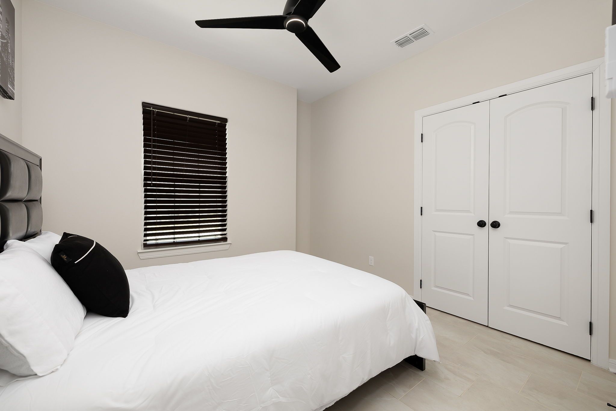 A bedroom with a bed, a ceiling fan, a window with blinds, and a white door.