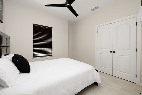 A bedroom with a bed, a ceiling fan, a window with blinds, and a white door.