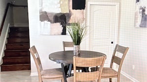 Un coin repas avec une table ronde, quatre chaises, un ventilateur de plafond et un escalier en arrière-plan.
