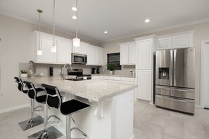 A modern kitchen with white cabinetry, stainless steel appliances, a granite countertop, and bar stools. - Casa Jerez - Near Padre Island, Church & Hospital (San Juan)